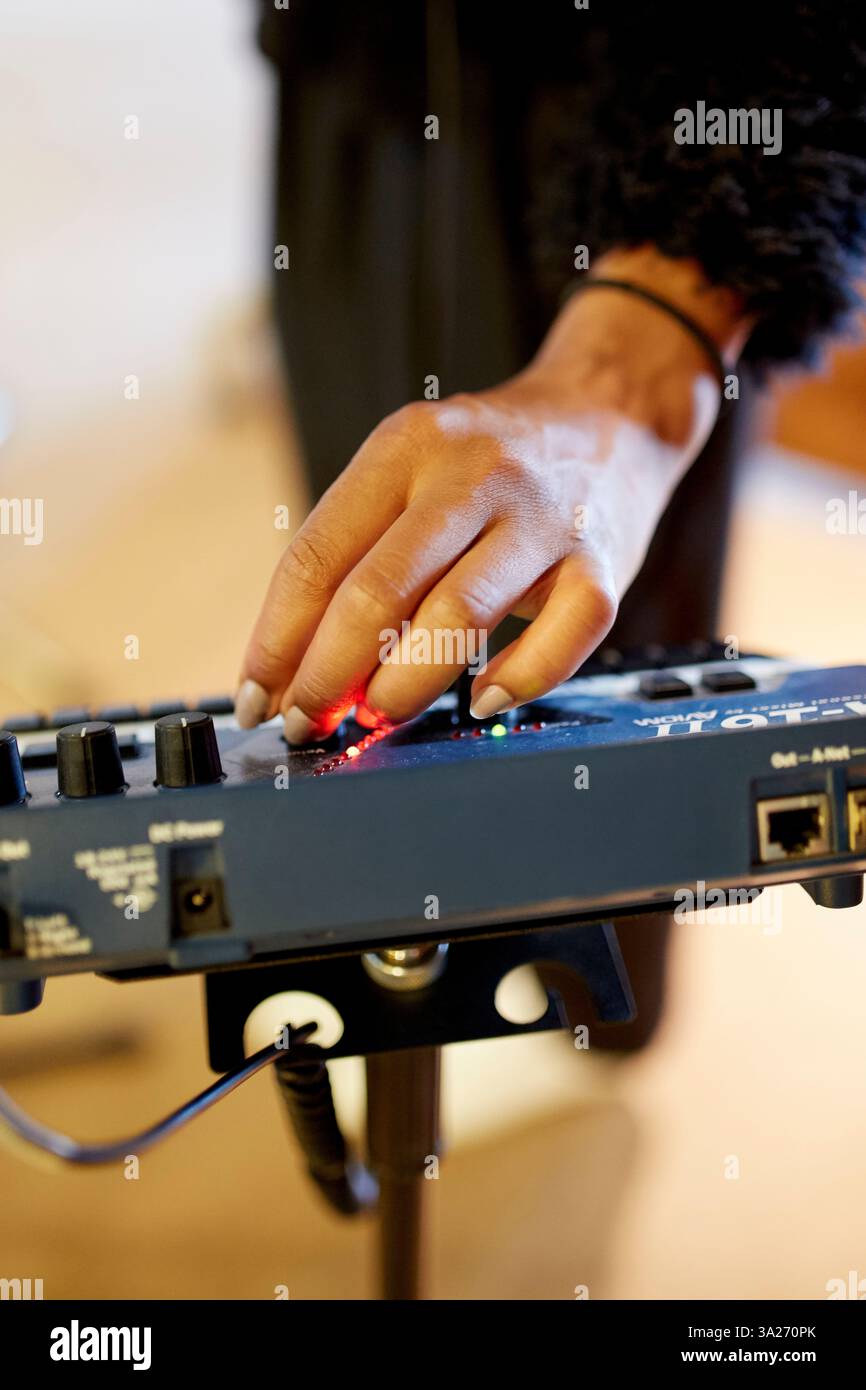Eine Hand stellt die Bedienelemente eines blauen Audiomischers in einem Aufnahmestudio ein, wobei die Regler und Leuchtanzeigen im Fokus stehen. Stockfoto