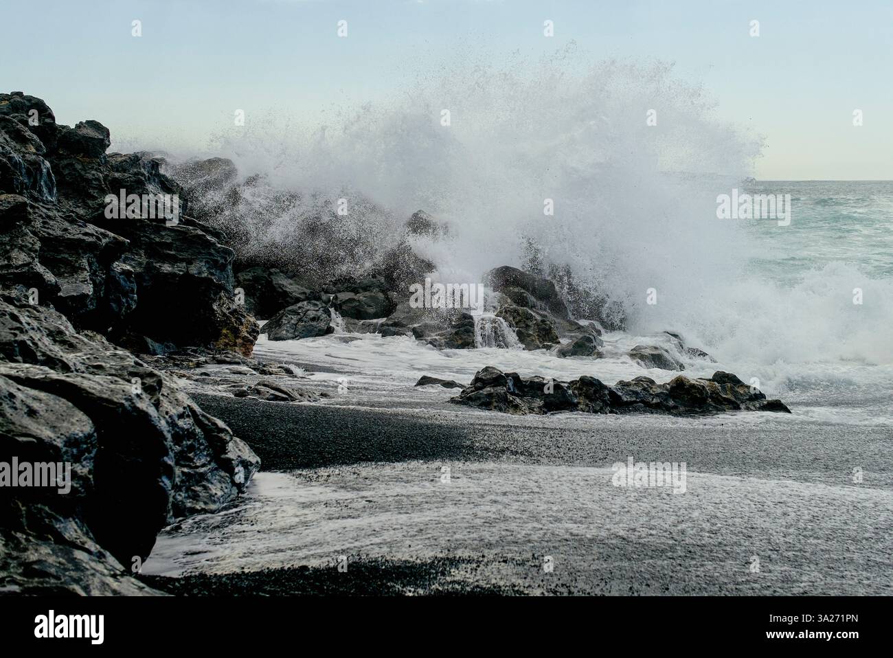 An einem bewölkten Küstentag krachen mächtige Meereswellen gegen schroffe schwarze Felsen. Lanzarote, Spanien Stockfoto