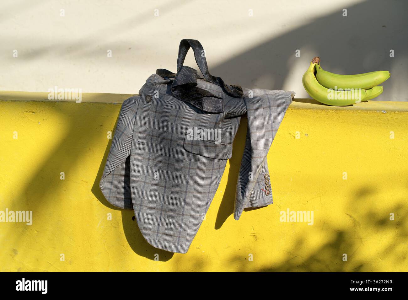 Graue karierte Jacke über einer gelben Betonwand mit zwei grünen Bananen daneben. Miami, FL, USA Stockfoto
