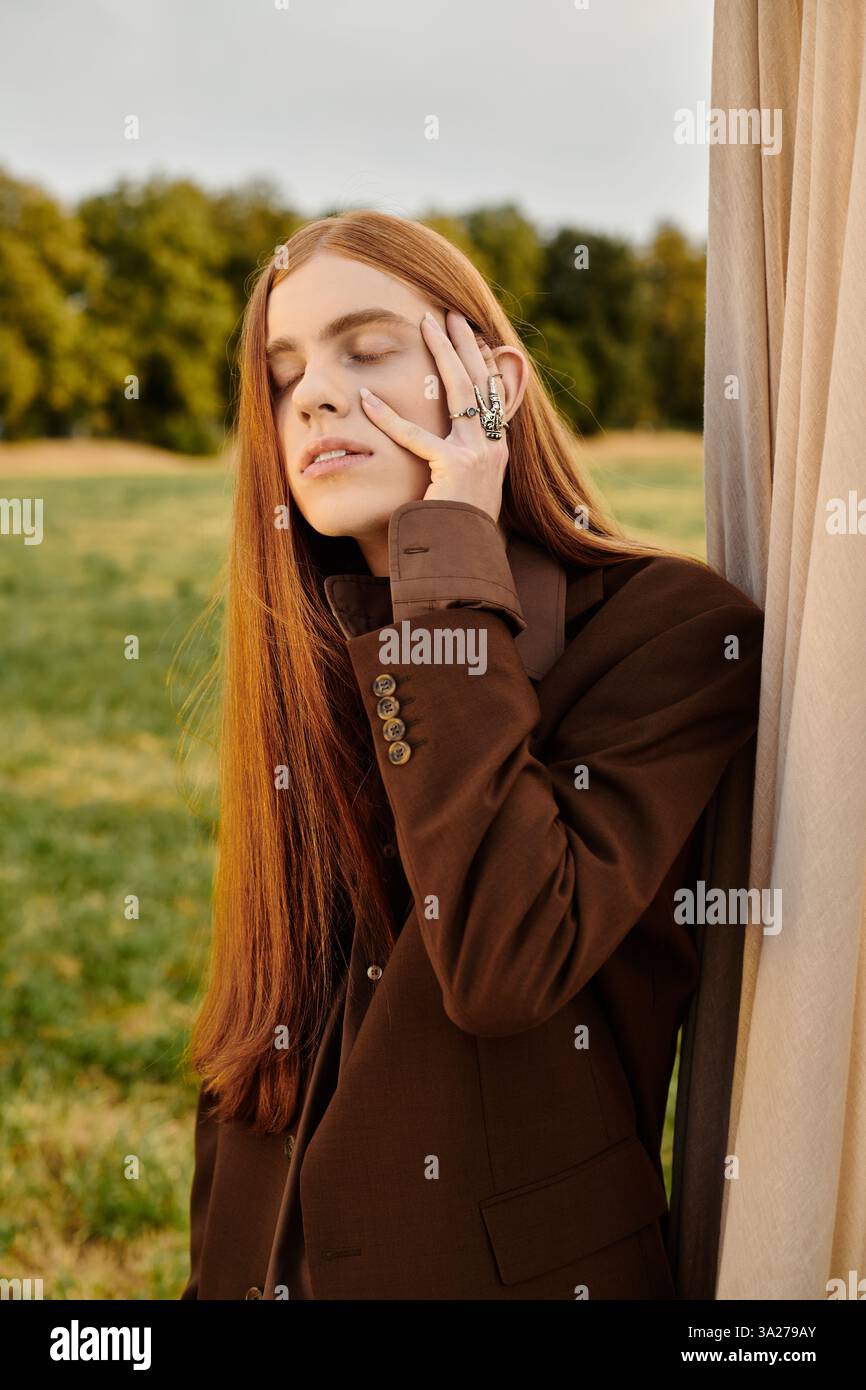 Ein schöner junger Mann in modischer Kleidung lehnt sich mit kontemplativem Ausdruck an einen Vorhang. Stockfoto