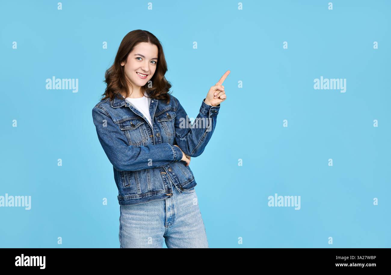 Porträt eines niedlichen Mädchens in einer Jeansjacke, der mit dem Finger zur Seite zeigt und Werbung zeigt. Isoliert auf blauem Hintergrund mit freiem Platz. Stockfoto
