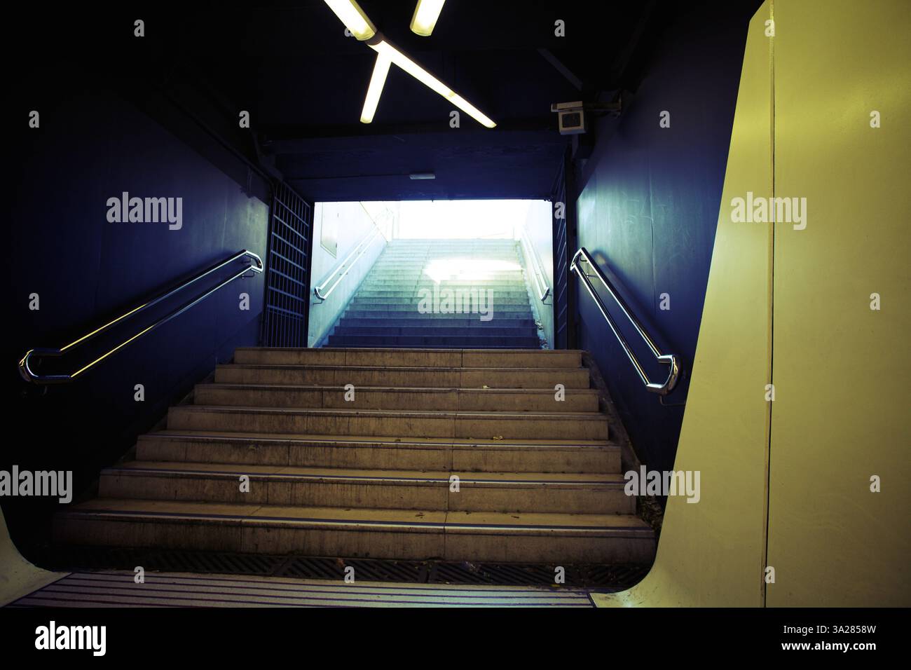 Blick auf eine Treppe, die zu einem hellen Ausgang führt, eingerahmt von dunklen Wänden und moderner Beleuchtung. Die Treppen sind aus Beton und die Atmosphäre ist städtisch und Stockfoto