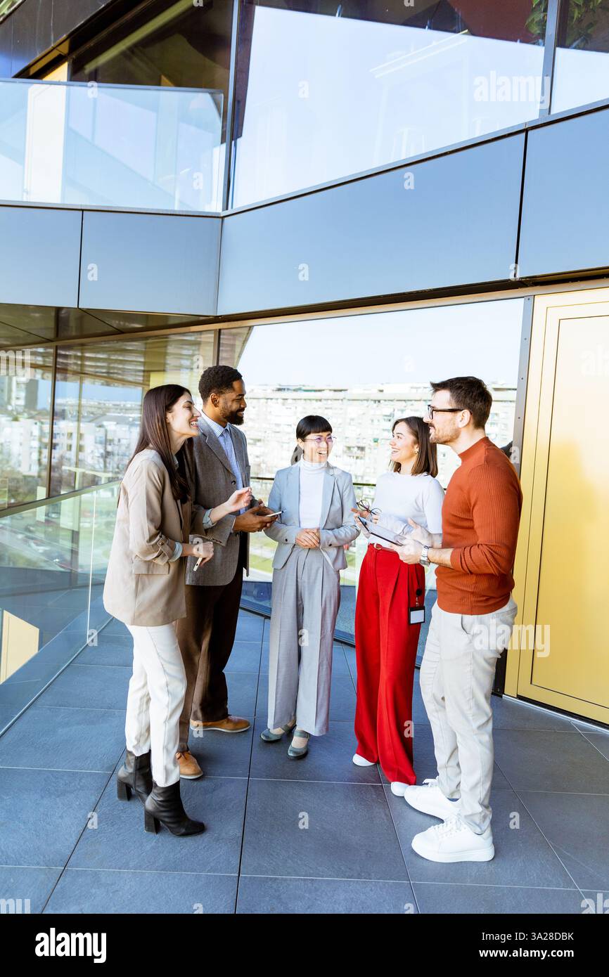 In einem eleganten Bürokorridor steht eine vielfältige Gruppe von Fachleuten, die während einer Networking-Veranstaltung Ideen austauschen und lachen. Das Ambiente ist lebhaft, fos Stockfoto