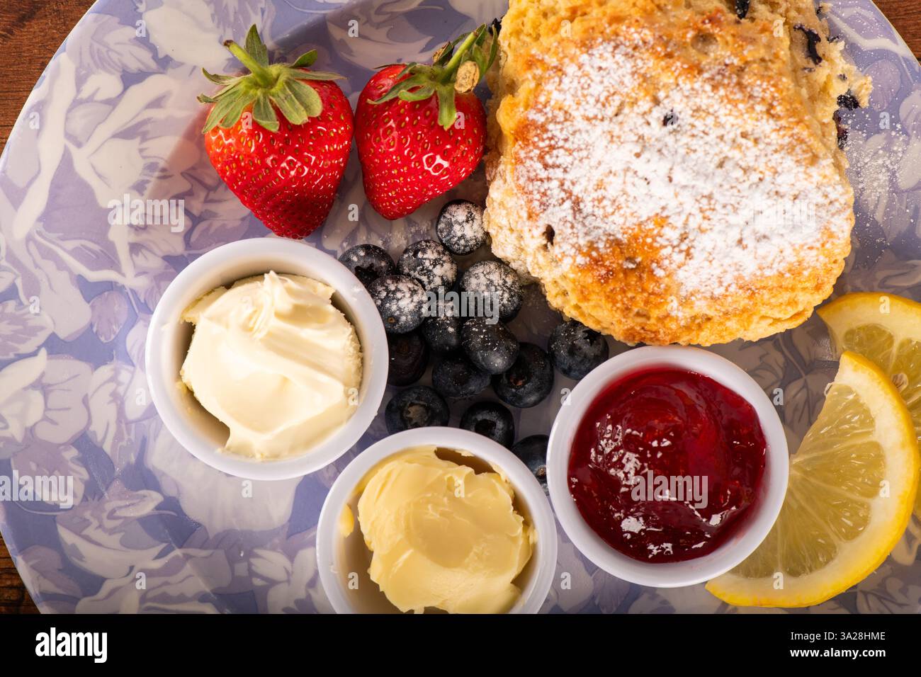 Ein Teller mit einem Zitronenkeil, Erdbeeren, Heidelbeeren und Marmelade. Die Platte ist blau und weiß Stockfoto