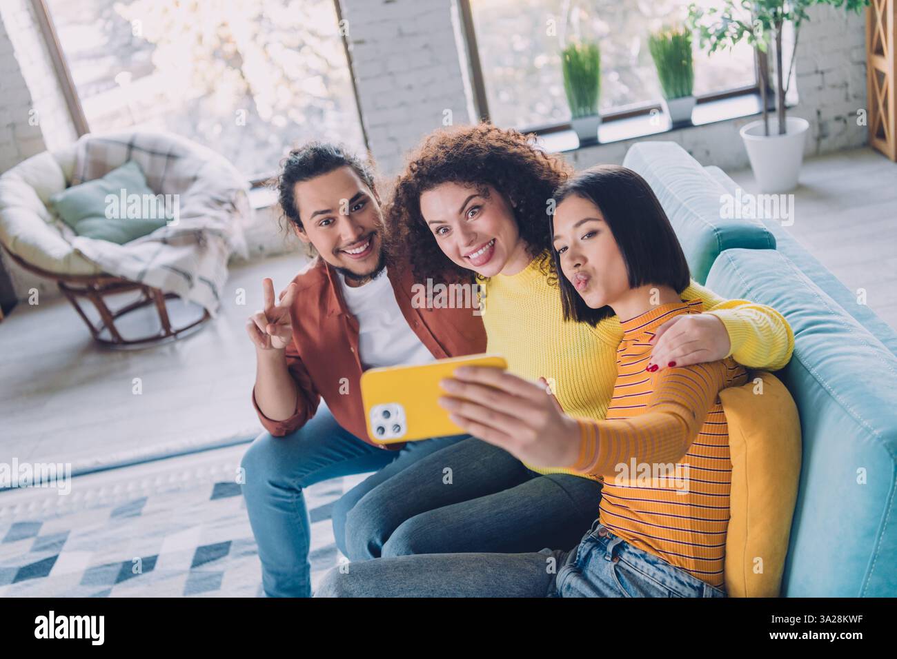 Eine Gruppe verschiedener Freunde macht ein Selfie auf der Couch in einem hellen Wohnzimmer, in dem Wärme, Freude und eine fröhliche Wochenendatmosphäre zum Ausdruck kommen. Stockfoto