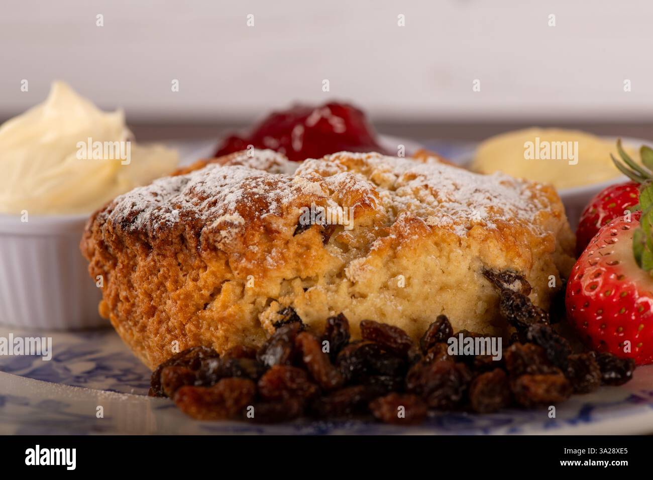 Ein Teller Obstscone mit einer Erdbeere darauf. Der Teller wird mit einer weißen Sauce und einer weißen Schüssel belegt Stockfoto