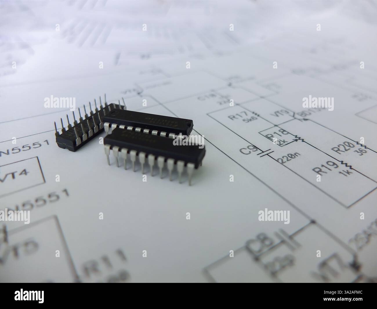 Verschiedene integrierte Schaltungen, Mikrocontroller in DIP-SOIC-TQFP-Gehäusen. Auf der Rückseite befindet sich ein Schaltplan Stockfoto