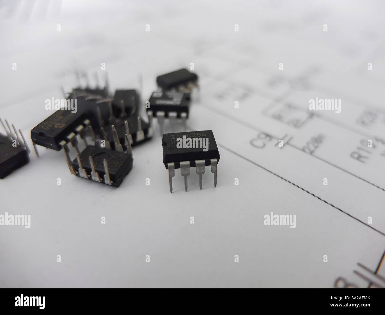 Verschiedene integrierte Schaltungen, Mikrocontroller in DIP-SOIC-TQFP-Gehäusen. Auf der Rückseite befindet sich ein Schaltplan Stockfoto