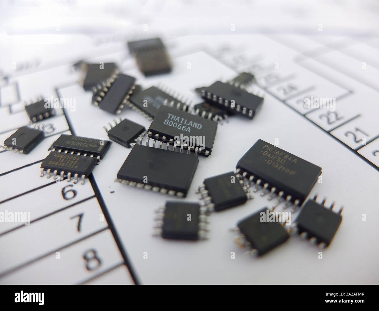 Verschiedene integrierte Schaltungen, Mikrocontroller in DIP-SOIC-TQFP-Gehäusen. Auf der Rückseite befindet sich ein Schaltplan Stockfoto