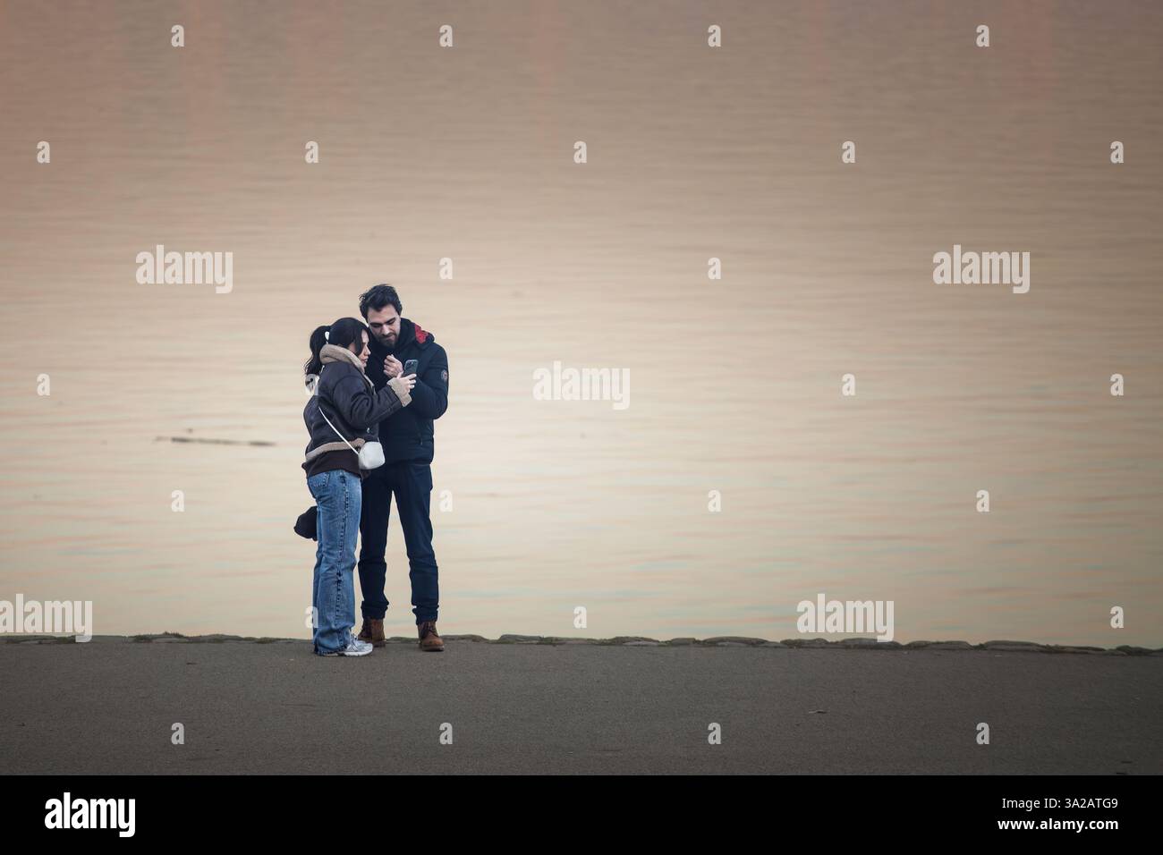 BELGRAD, SERBIEN - 12. OKTOBER 2024: Ein Paar, das ein Smartphone an der Donau in Zemun, Belgrad, benutzt, um moderne Beziehungen zu veranschaulichen Stockfoto