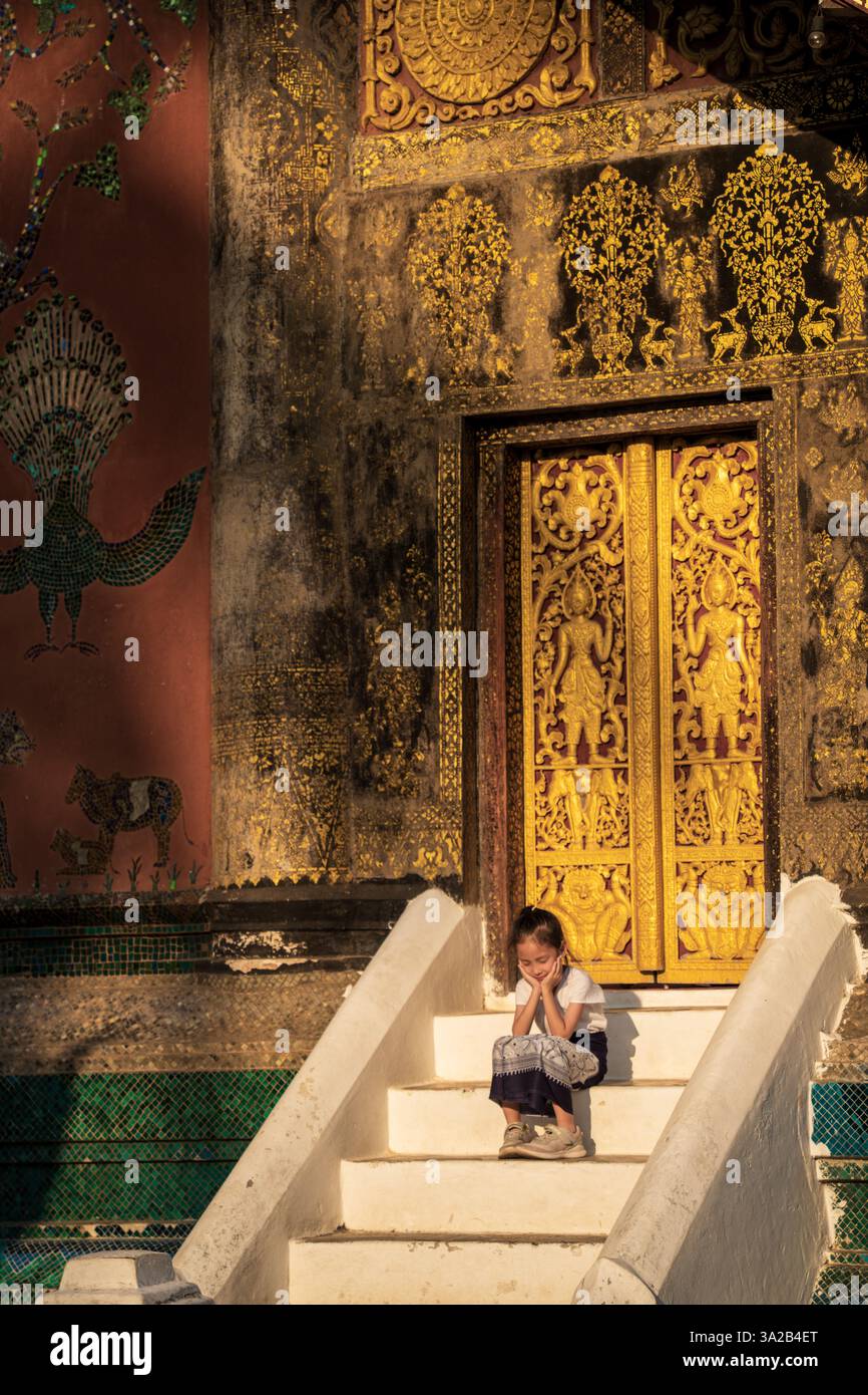 Mädchen sitzt im Wat Xieng Thong, Luang Prabang, Laos. Tempelarchitektur, kulturelles Moment Stockfoto