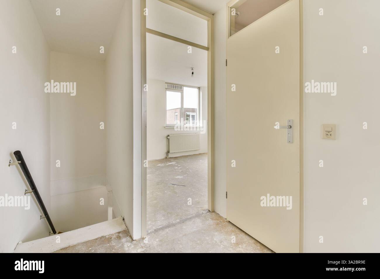 Ein minimalistischer Innenraum verfügt über eine offene Tür, die zu einer Treppe führt, die helle weiße Wände und ein Gefühl von Offenheit bietet. Stockfoto