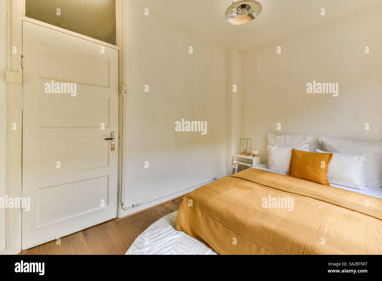 Ein gemütliches, minimalistisches Zimmer in warmen Farben mit einem einfachen Bett, weißen Wänden und natürlichem Licht, das komfortable Essentials bietet. Stockfoto