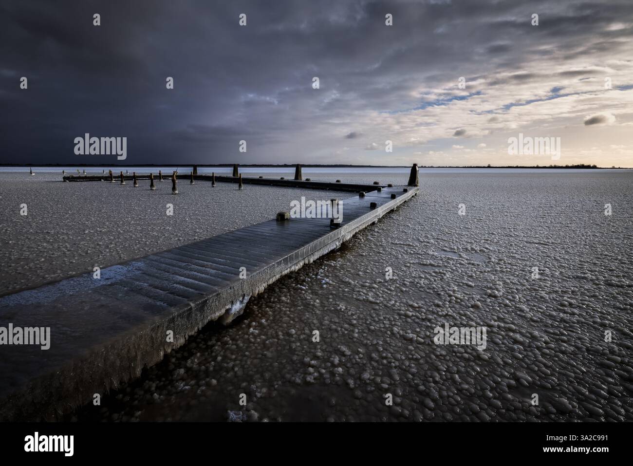 Ein kalter Wintersonnenaufgang über dem Lauwersmeer. Das Wasser ist gefroren und der Pier ist mit Eis bedeckt. Stockfoto