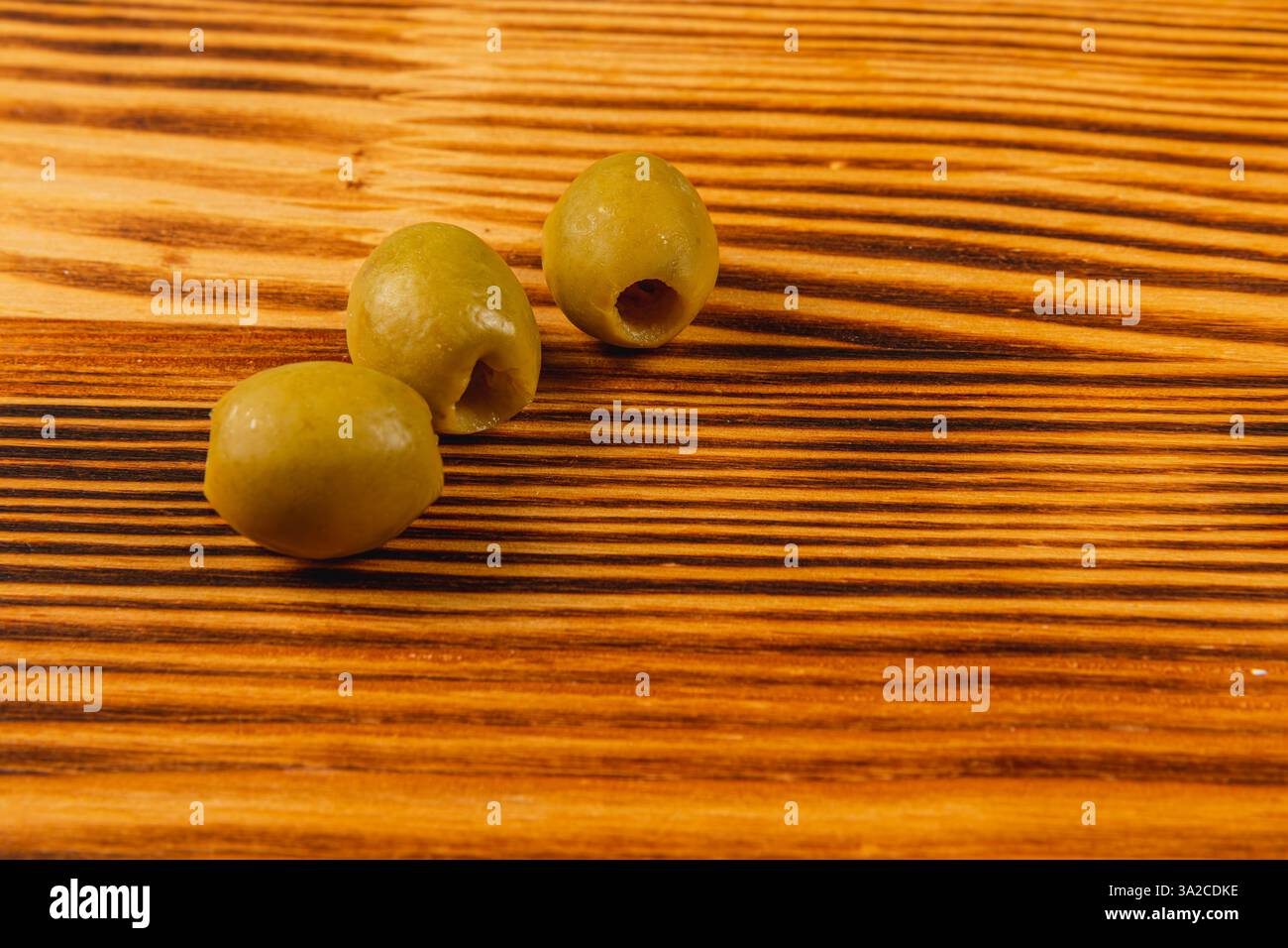 Drei grüne Oliven liegen auf einer Holzoberfläche und zeigen ihre glatte Textur. Die warmen Holztöne schaffen eine gemütliche Atmosphäre, die ein Gefühl von einlädt Stockfoto