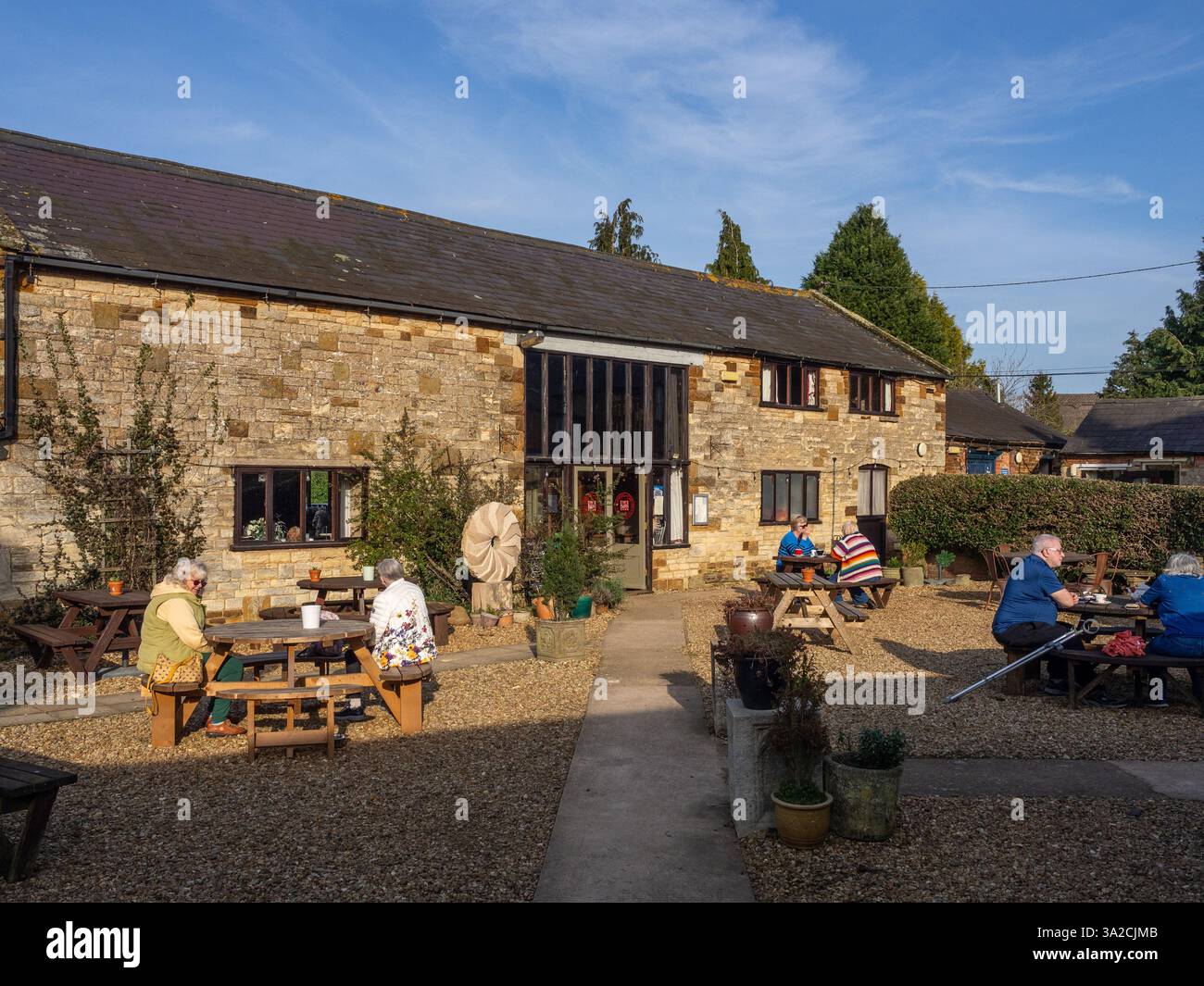 Gäste im Barn Cafe genießen Wintersonne, Upper Stowe Dairy Farm, Northamptonshire, Großbritannien Stockfoto