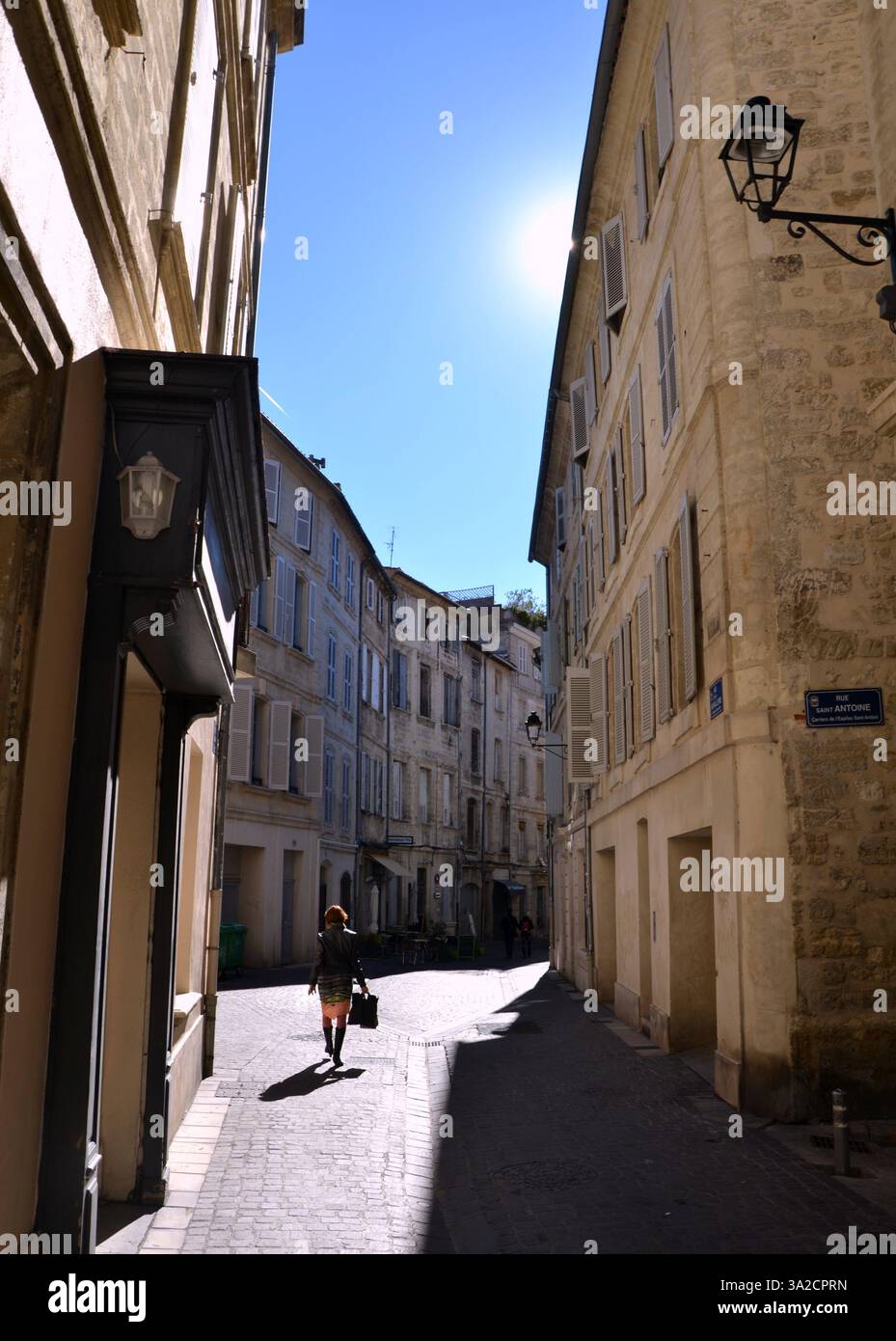 Eine Frau läuft durch eine Straße in der Mittagssonne in Avignon, Frankreich Stockfoto