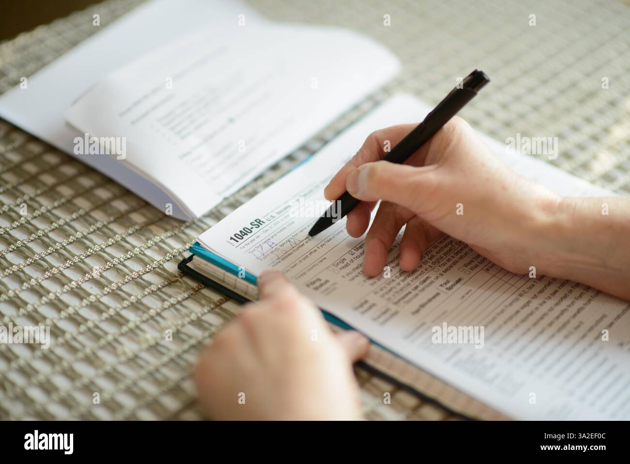 Eine ältere Frau, die an einem Tisch saß und ihr Steuerformular 1040-SR sorgfältig mit einem Stift ausfüllte. Das Home-Setting unterstreicht die persönliche Finanzorganisation Stockfoto