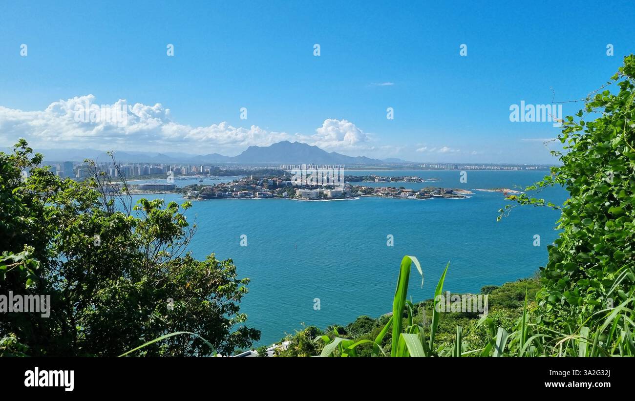 Pulsierendes blaues Wasser erstreckt sich über den Rahmen und umgibt eine Insel mit eleganten Häusern und üppigem Grün. - Smartphone-aufgenommenes Stockfoto