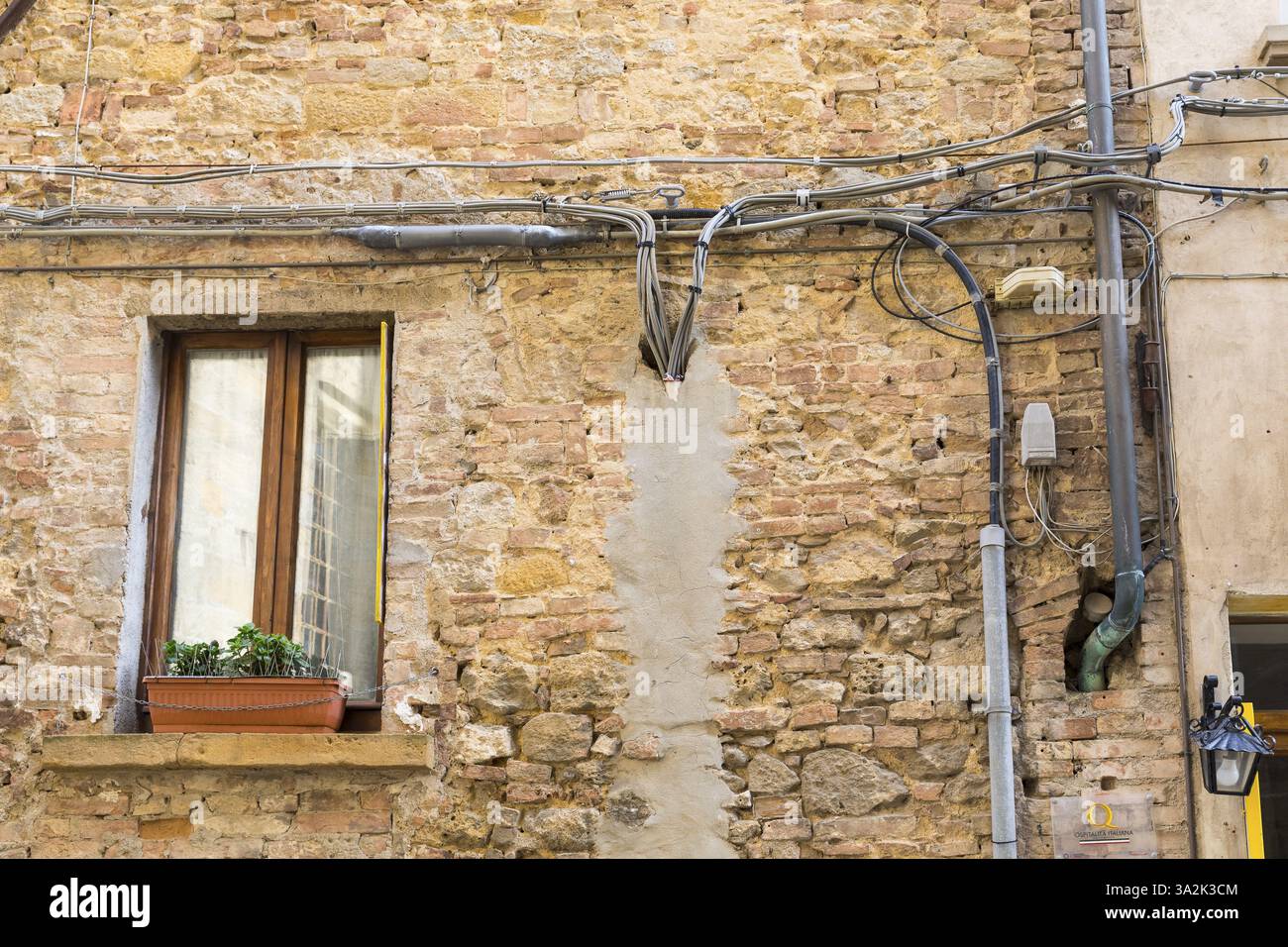 Hauswand mit freiliegenden Stromkabeln, Löchern und teilweise verputzt im historischen Zentrum von Volterra, Provinz Pisa, Toskana, Italien, Europa Stockfoto