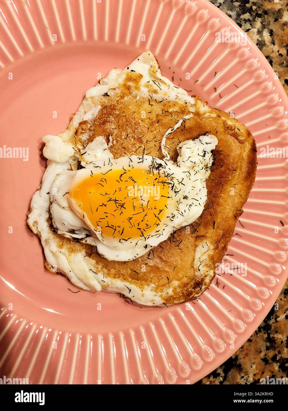 Rosa Teller mit einem Ei auf Toast, garniert mit Dill. Blick von oben, goldbraunes Brot und gesprenkelter Hintergrund Stockfoto