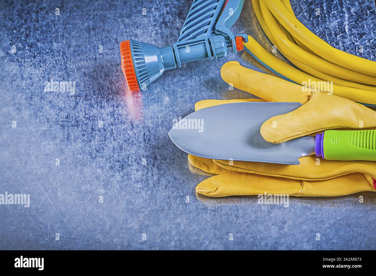 Gummi Gartenschlauch Sprühdüse Schutzhandschuhe Handschaufel auf metallischem Hintergrund Gartenkonzept Stockfoto