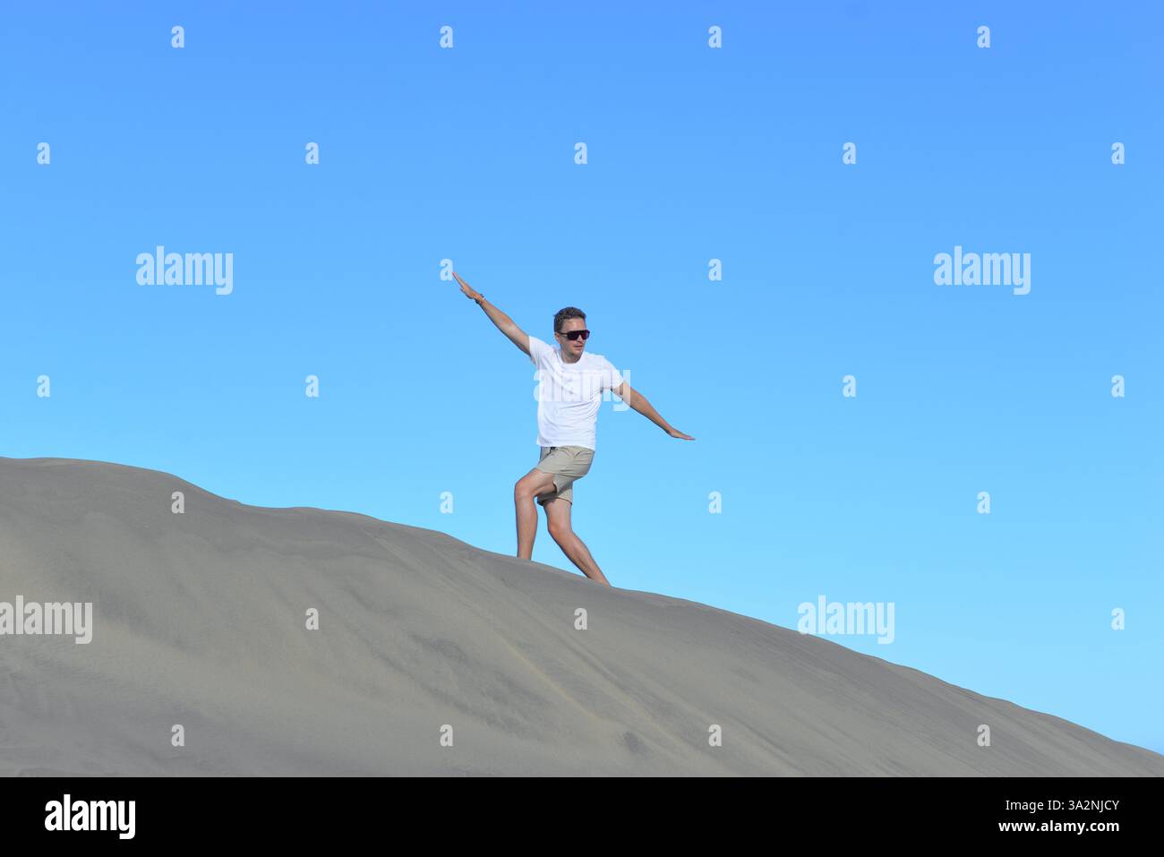 Ein junger Mann, der an einem heißen, sonnigen Tag auf einer Sanddüne durch Barhan in Maspalomas, Gran Canaria, spaziert. Ein selbstbewusster Mann geht den Berg hinauf Stockfoto