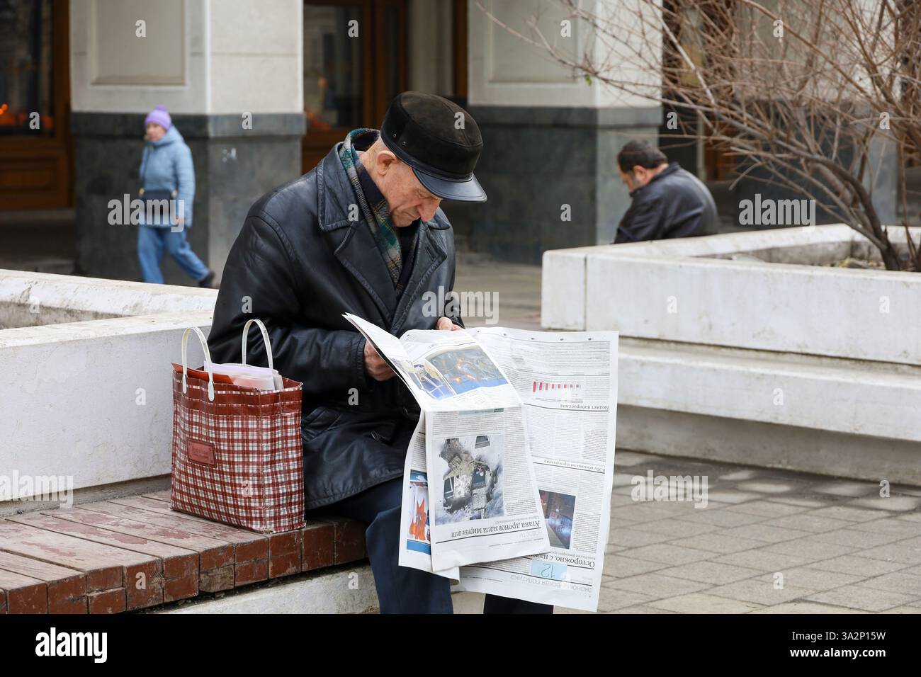 Ein alter Mann liest Zeitung auf der Straßenbank der Stadt Stockfoto
