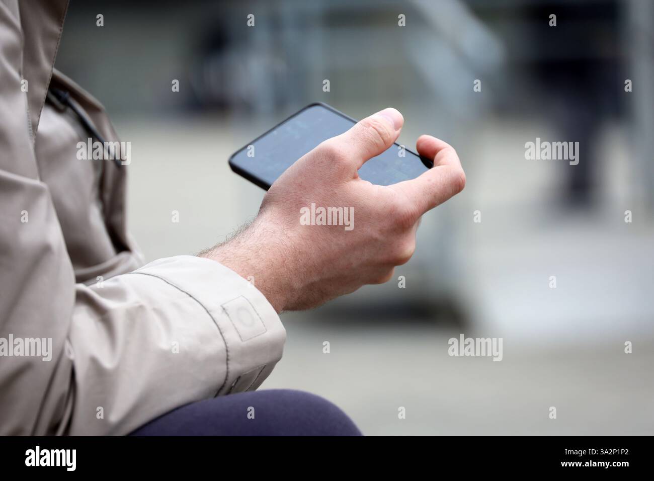 Smartphone in den Händen eines Mannes, der auf der Straße sitzt. Videos ansehen und Spiele im Freien spielen Stockfoto