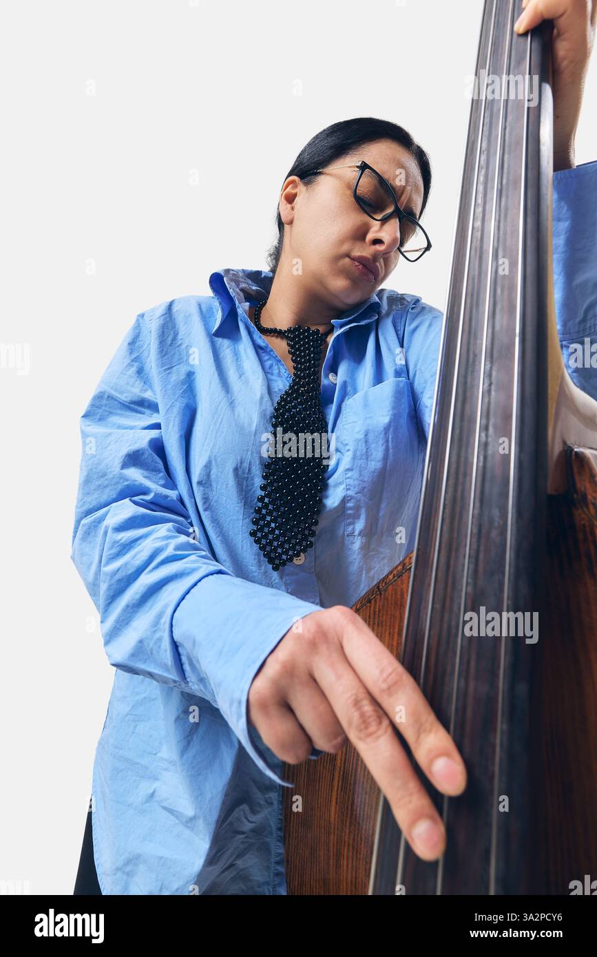 Engagierter Musiker im übergroßen blauen Hemd, der Kontrabass mit roher Emotion und Konzentration spielt. Stockfoto