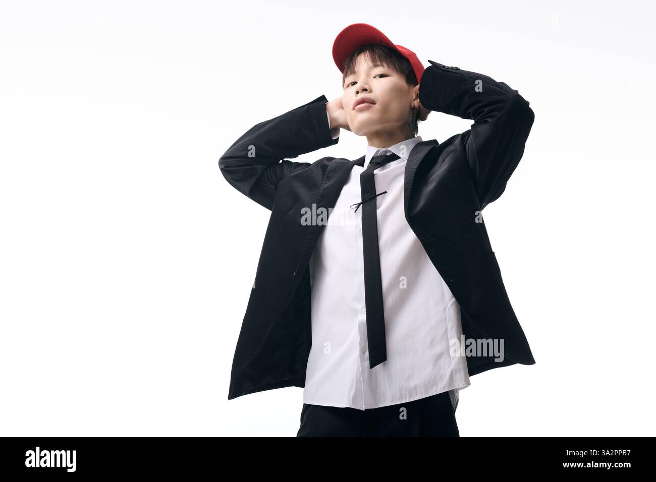 Ein junger, attraktiver asiatischer Mann, der in einem schicken Outfit gekleidet ist, posiert selbstbewusst mit einem lässigen Hut. Stockfoto