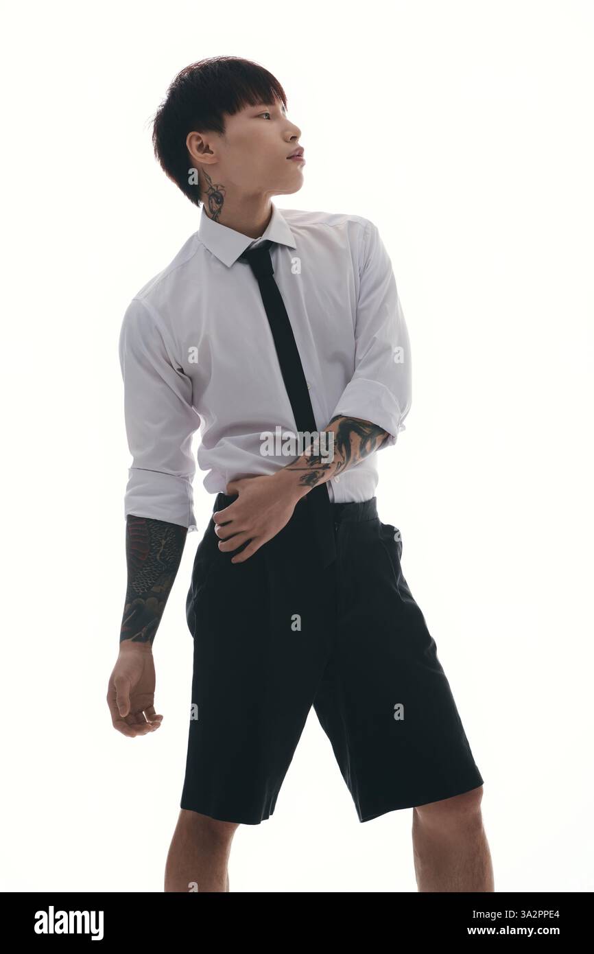 Selbstbewusster junger Mann mit Tattoos posiert in einem eleganten Outfit, der Kreativität und Stil zum Ausdruck bringt. Stockfoto