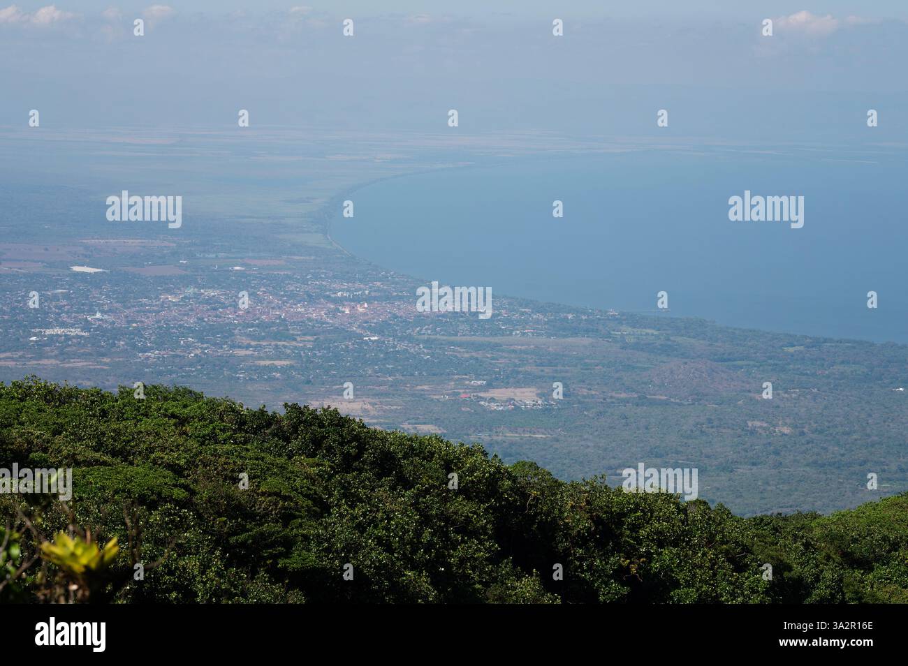 Weitläufiger Blick auf die Küste mit üppigem Grün, Meer und entfernter Stadt unter klarem Himmel während des Tages. Stockfoto