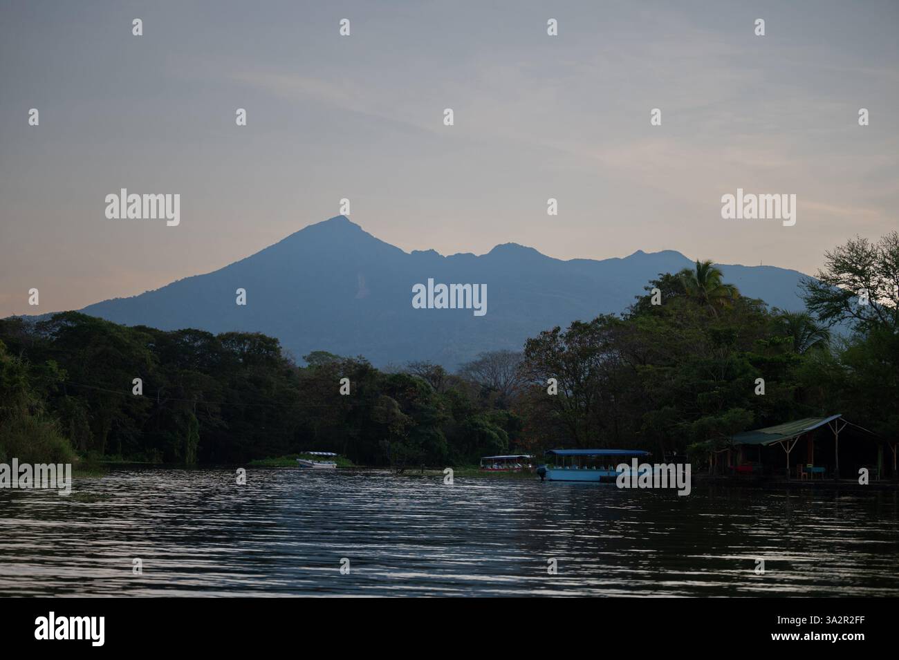 Ein ruhiger Fluss reflektiert das schwindende Licht, während ein majestätischer Berg in der Abenddämmerung, umgeben von der Natur, bewacht. Stockfoto