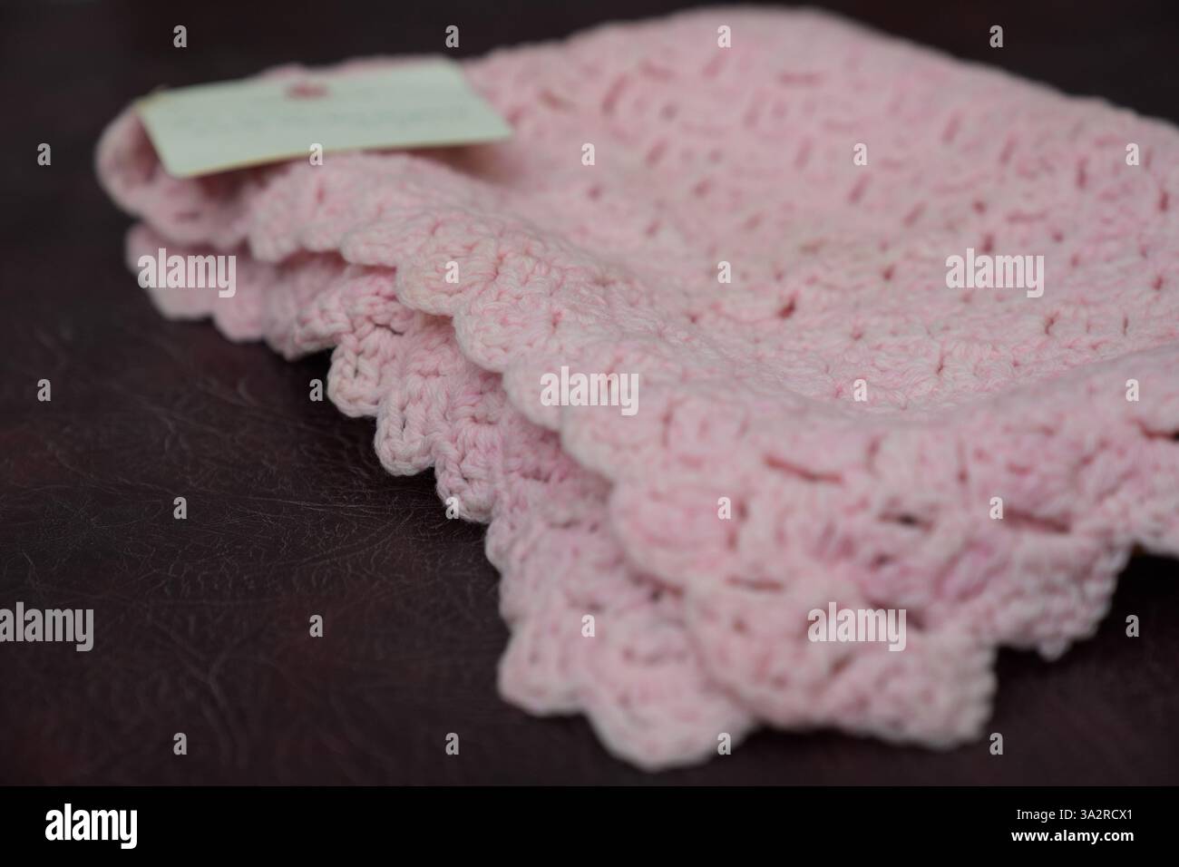 Eine pinkfarbene Babydecke, die vor fast 100 Jahren von Queen Mary bei Hansons Auctioneers in Etwall, Derbyshire, hergestellt wurde, bevor sie am Freitag zur Auktion aufsteigt. Die von Queen Mary gefertigte Häkeldecke trägt noch immer das Etikett „Made by her Majesty the Queen“ im Buckingham Palace. Sie wurde von der Verkäuferin im Haus ihrer 93-jährigen Tante in Wimbledon, Süd-London, entdeckt, aber keiner weiß, woher sie kam. Bilddatum: Mittwoch, 25. September 2024. Stockfoto