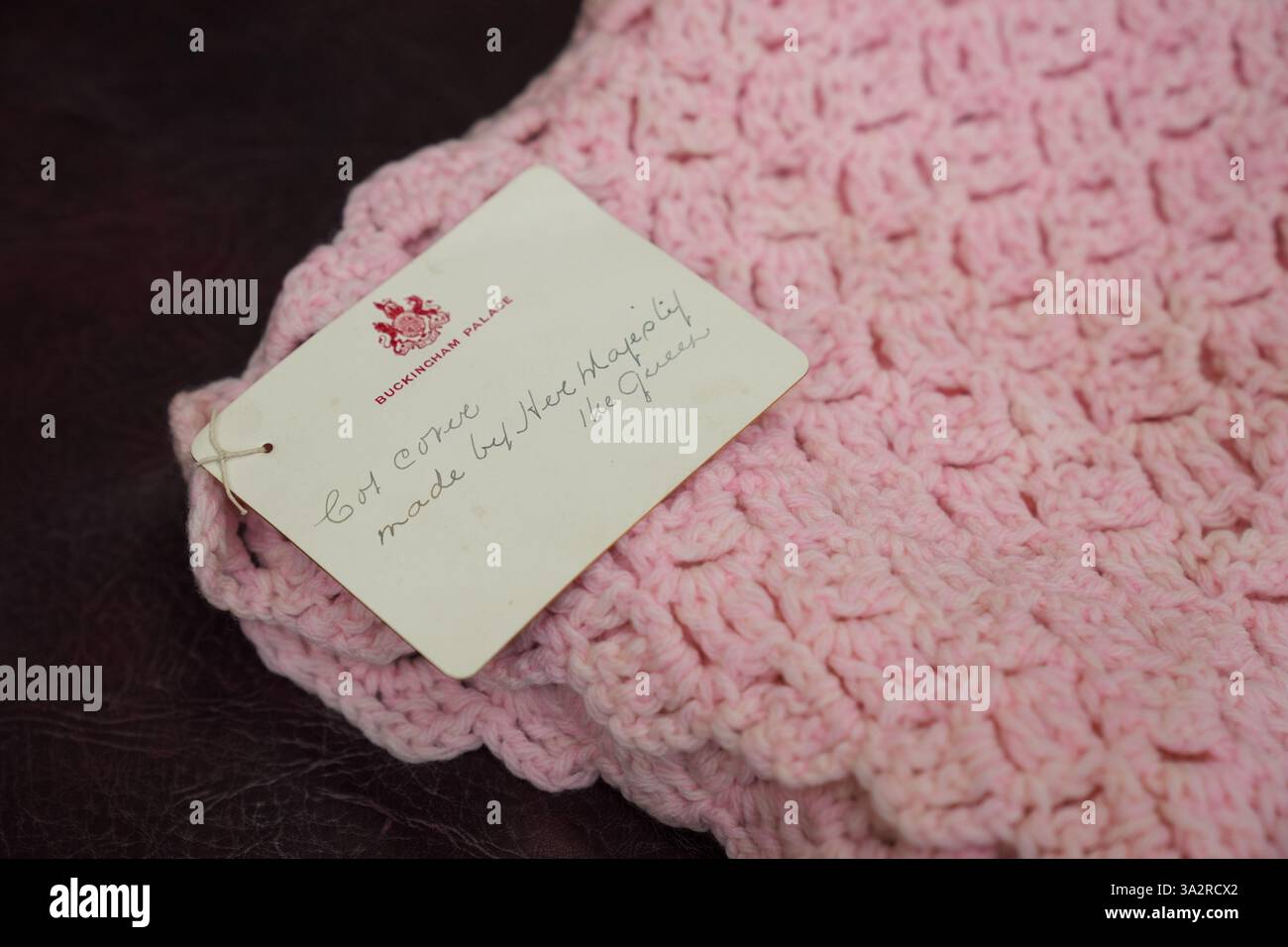 Eine pinkfarbene Babydecke, die vor fast 100 Jahren von Queen Mary bei Hansons Auctioneers in Etwall, Derbyshire, hergestellt wurde, bevor sie am Freitag zur Auktion aufsteigt. Die von Queen Mary gefertigte Häkeldecke trägt noch immer das Etikett „Made by her Majesty the Queen“ im Buckingham Palace. Sie wurde von der Verkäuferin im Haus ihrer 93-jährigen Tante in Wimbledon, Süd-London, entdeckt, aber keiner weiß, woher sie kam. Bilddatum: Mittwoch, 25. September 2024. Stockfoto