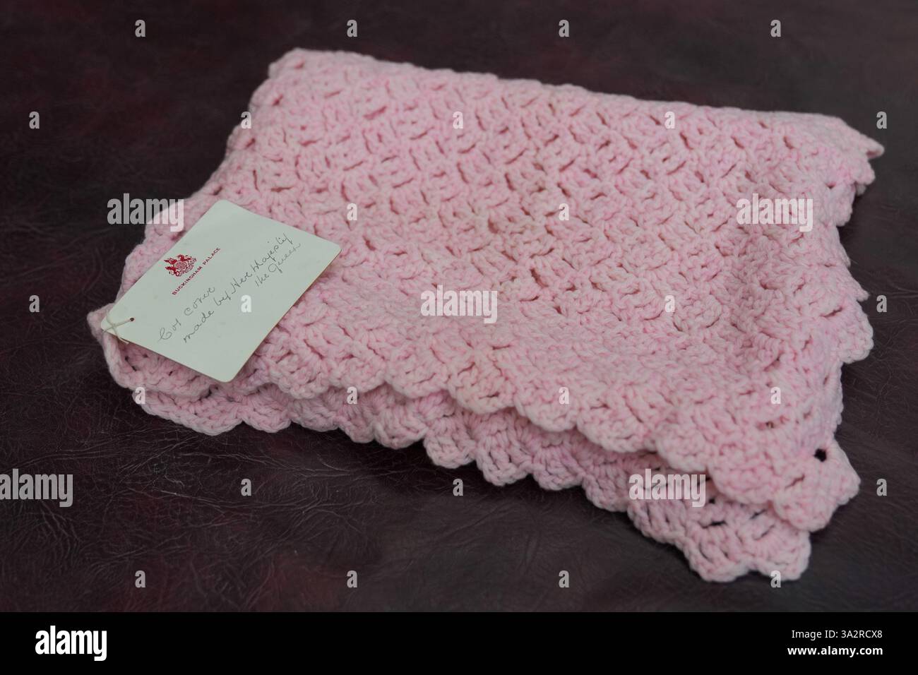 Eine pinkfarbene Babydecke, die vor fast 100 Jahren von Queen Mary bei Hansons Auctioneers in Etwall, Derbyshire, hergestellt wurde, bevor sie am Freitag zur Auktion aufsteigt. Die von Queen Mary gefertigte Häkeldecke trägt noch immer das Etikett „Made by her Majesty the Queen“ im Buckingham Palace. Sie wurde von der Verkäuferin im Haus ihrer 93-jährigen Tante in Wimbledon, Süd-London, entdeckt, aber keiner weiß, woher sie kam. Bilddatum: Mittwoch, 25. September 2024. Stockfoto
