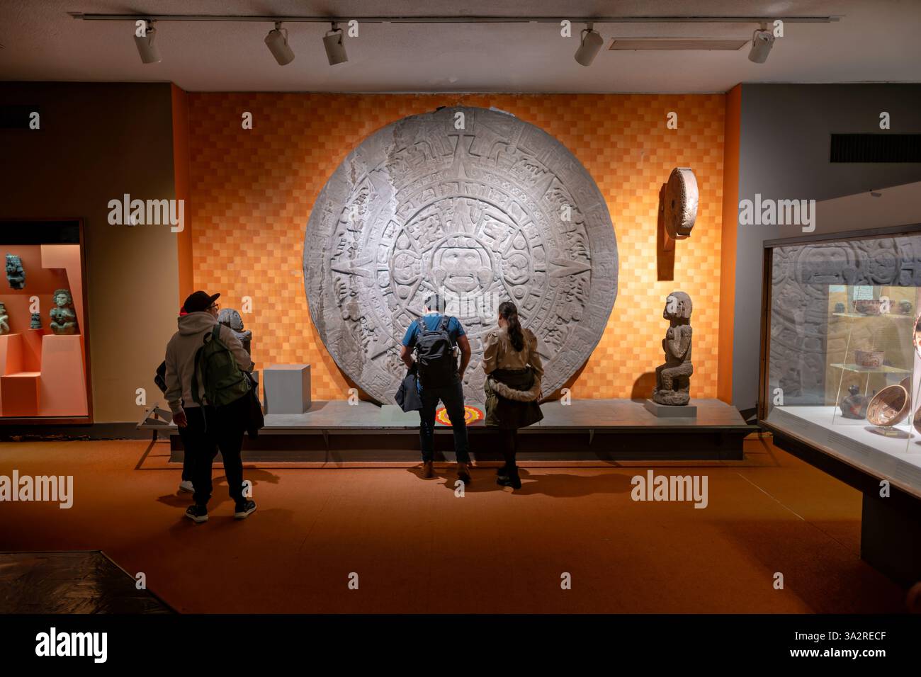 Aztec Stone of the Sun American Museum of Natural History New York City // NEW YORK, Vereinigte Staaten — Eine vollständige Reproduktion des Aztec Stone of the Sun ist im American Museum of Natural History ausgestellt. Die Replik repräsentiert den ursprünglichen 20 Tonnen schweren Porphyr-Monolithen, der 1790 entdeckt wurde und einen Durchmesser von etwa 12 Fuß hat und komplexe Sonnensymboliken aufweist, die für aztekische Glaubenssätze von zentraler Bedeutung sind. Ursprünglich im zeremoniellen Zentrum von Tenochtitlan installiert, befindet sich der eigentliche Stein der Sonne heute im Nationalmuseum für Anthropologie von Mexiko-Stadt, während dieses detaillierte r Stockfoto