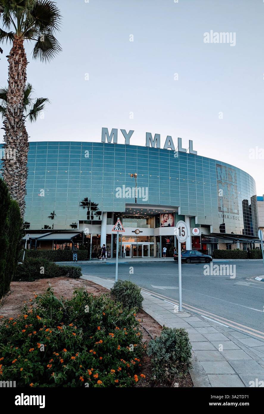 Außenansicht der My Mall in Limassol, Zypern, mit seiner modernen Glasfassade und dem von Palmen gesäumten Eingang in der Abenddämmerung. Stockfoto