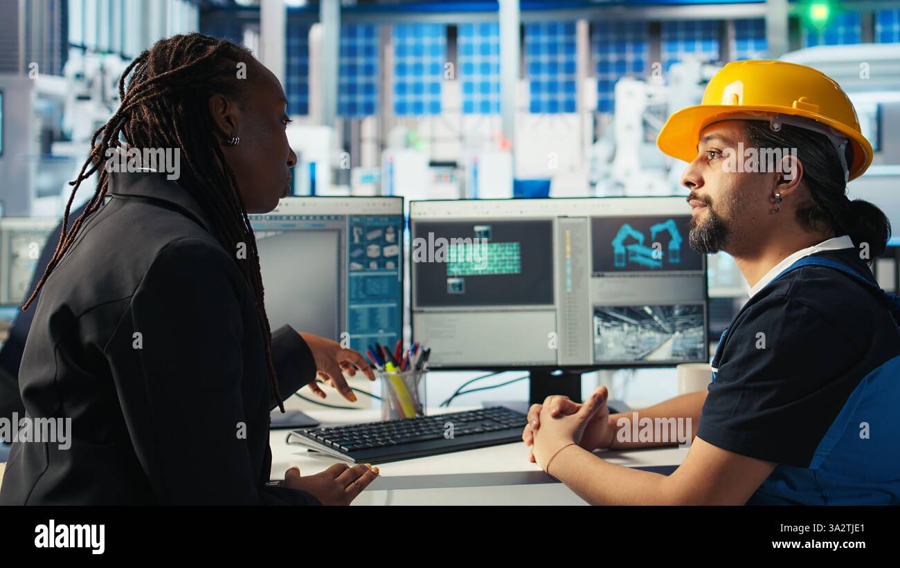 Arbeiter in der Photovoltaik-Fabrik diskutiert mit Frau über die Systemleistung. Produktionsanlage für Solarpaneele afroamerikanischer Manager im Gespräch mit Ingenieur über Energieerzeugung, Kamera A Stockfoto