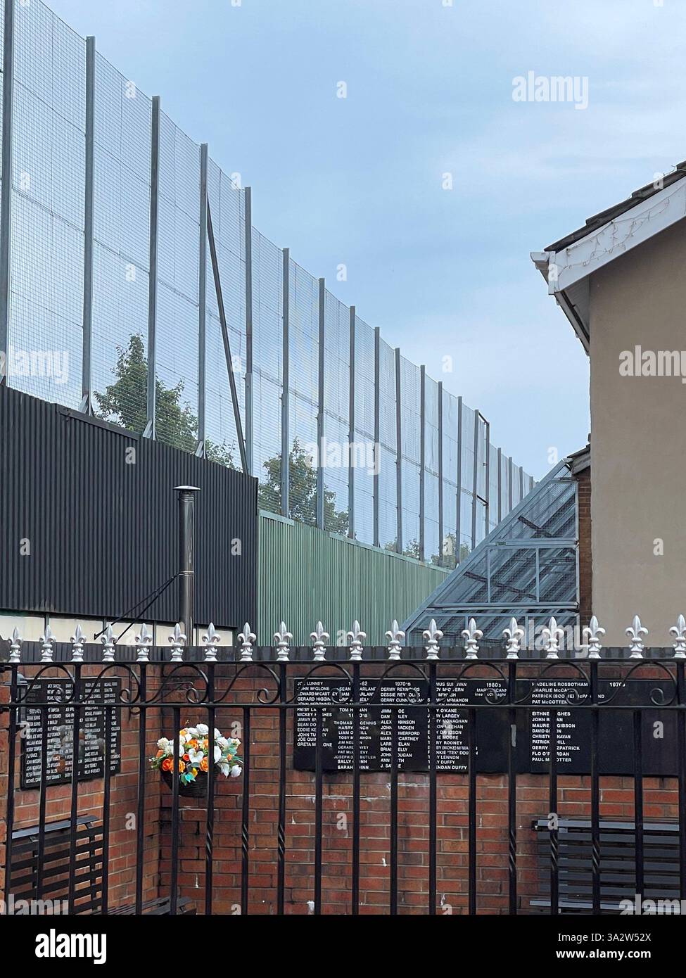 Ein Abschnitt der Friedensmauer von Belfast mit einem Denkmal hinter eisernen Geländern, das die geteilte Vergangenheit der Stadt symbolisiert. Stockfoto