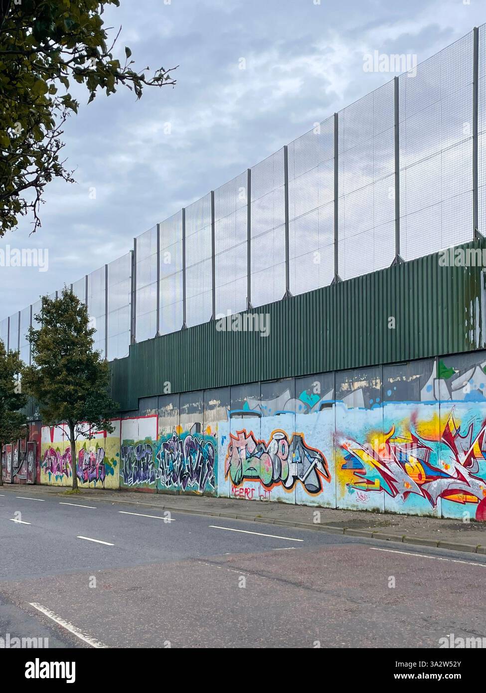 Ein Abschnitt der Friedensmauer von Belfast mit einem Denkmal hinter eisernen Geländern, das die geteilte Vergangenheit der Stadt symbolisiert. Stockfoto
