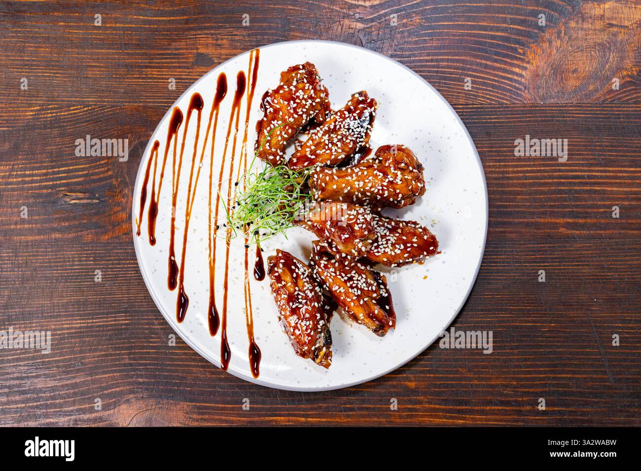 Ein Teller mit saftigen Hähnchenflügeln, überzogen mit einer glänzenden Glasur, bestreut mit Sesamsamen und garniert mit frischen Kräutern, um ein appetitliches Presen zu schaffen Stockfoto