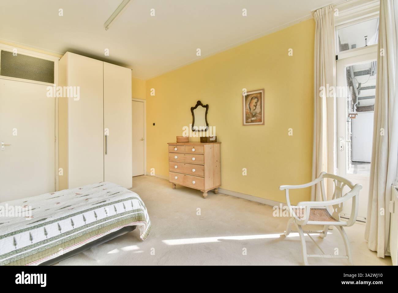 Ein ruhiges und minimalistisches Schlafzimmer mit gelben Wänden, einfachen Möbeln und natürlichem Licht schafft eine gemütliche Atmosphäre zum Entspannen. Stockfoto