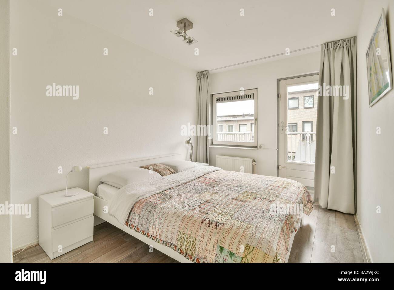 Ein modernes, stilvolles Schlafzimmer mit einem einfachen Bett, hellen Wänden und viel Tageslicht durch ein Fenster für eine ruhige Atmosphäre. Stockfoto