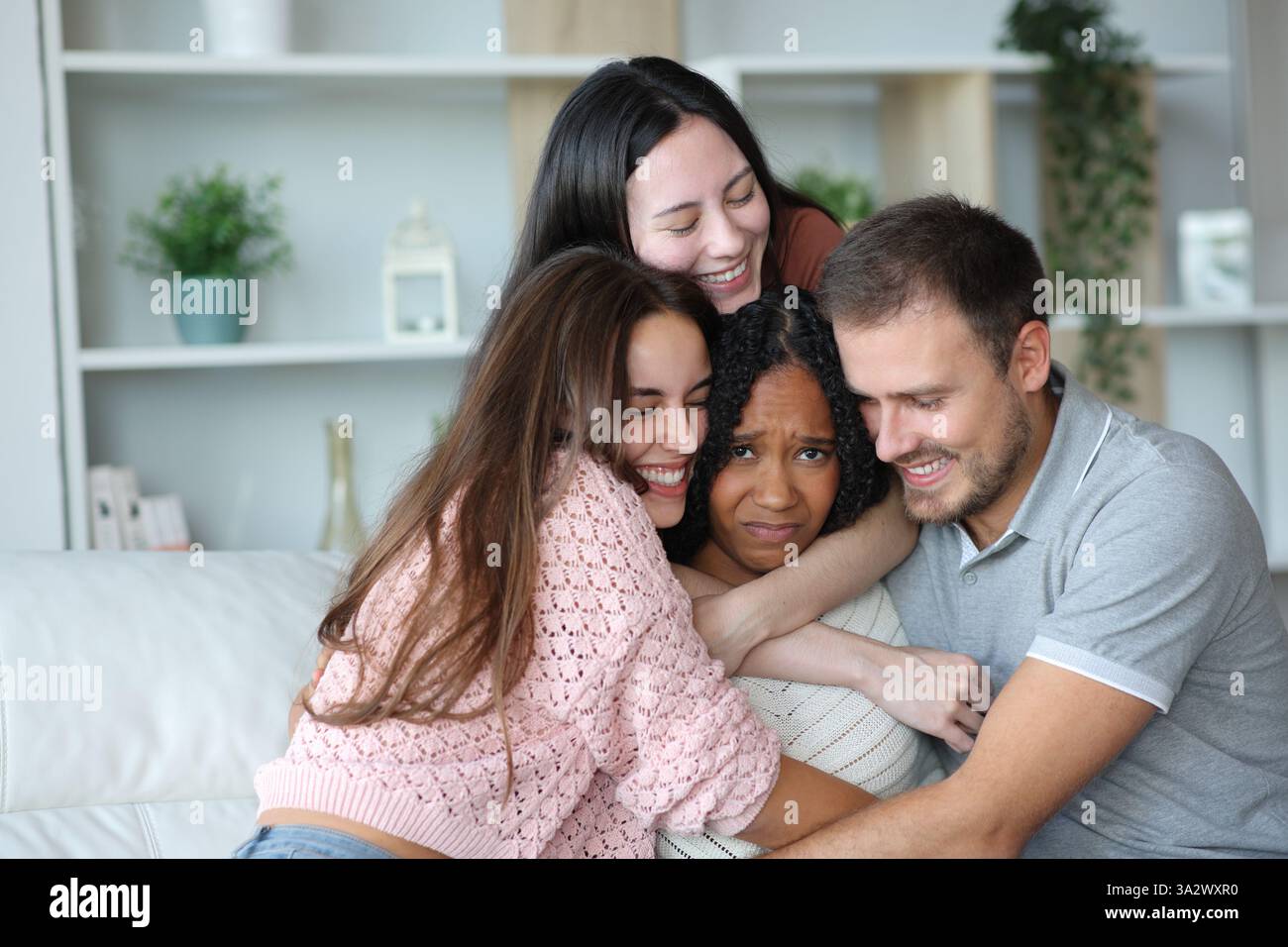 Überforderte Frau, die von Freunden umarmt wird, die zu Hause in die Kamera schauen Stockfoto