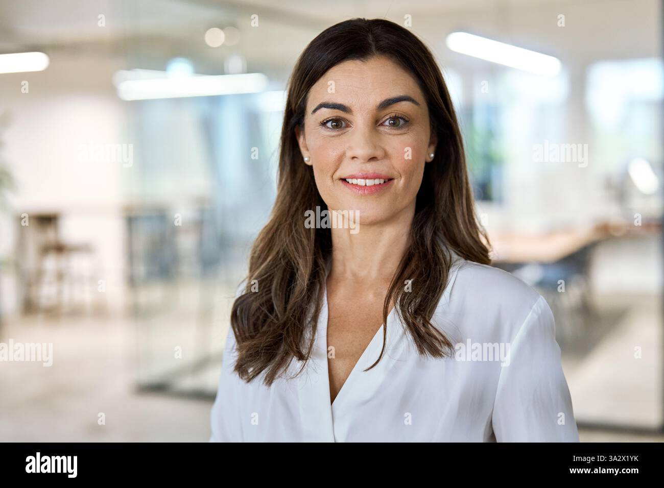 Glückliche Geschäftsfrau mittleren Alters, die im Büro steht und in die Kamera blickt. Kopfschuss. Stockfoto