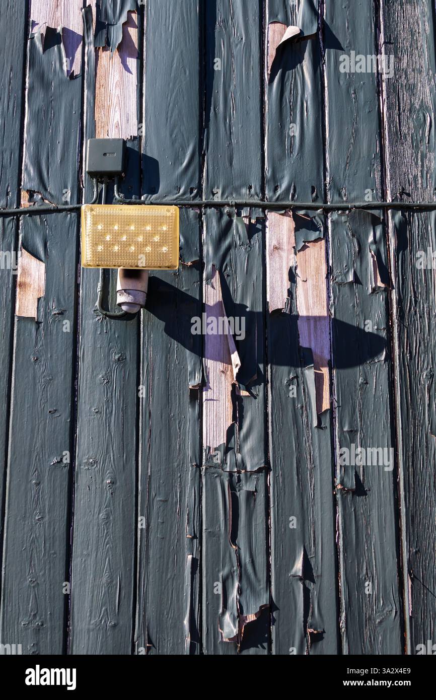 Grüne Farbe, die von einer Holzdielen-Fassade abblättert, über die ein elektrisches Kabel verläuft, ebenfalls mit derselben verwitterten Schicht beschichtet, was das Alter deutlich macht Stockfoto
