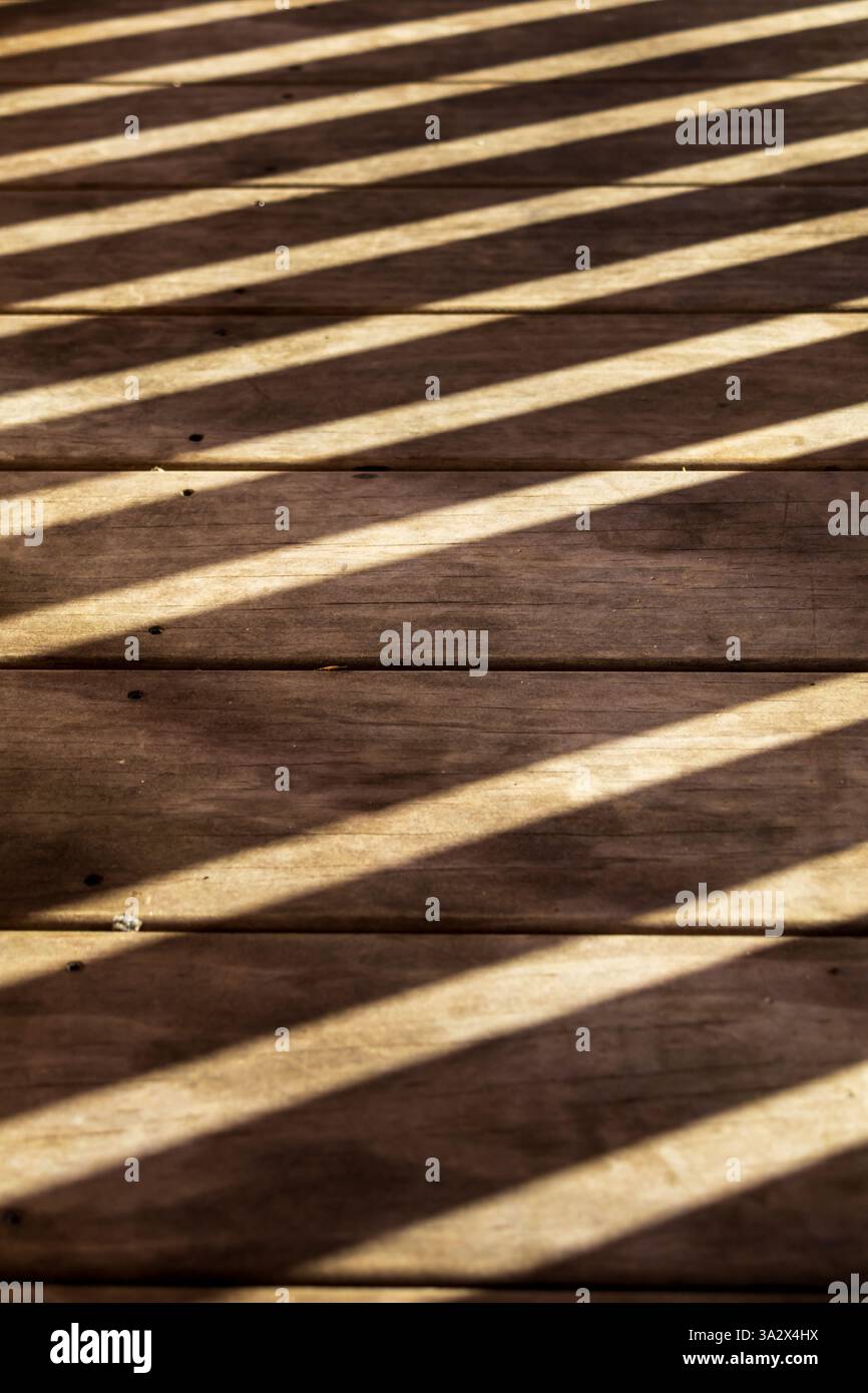 Diagonale, parallele Schatten von einem Geländer fallen über einen Holzboden im Freien, wo glatte Dielen horizontal in perfekter Ausrichtung mit dem Schuss verlaufen Stockfoto