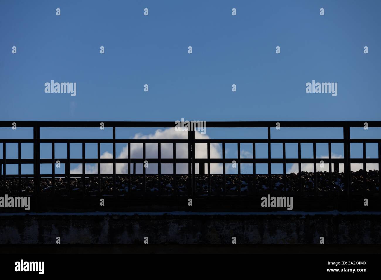 Von unten fotografiert, bildet eine Zementbrücke mit Metallgeländern sich kreuzende Quadrate und Rechtecke in Silhouette, die vor einem klaren blauen Himmel stehen Stockfoto